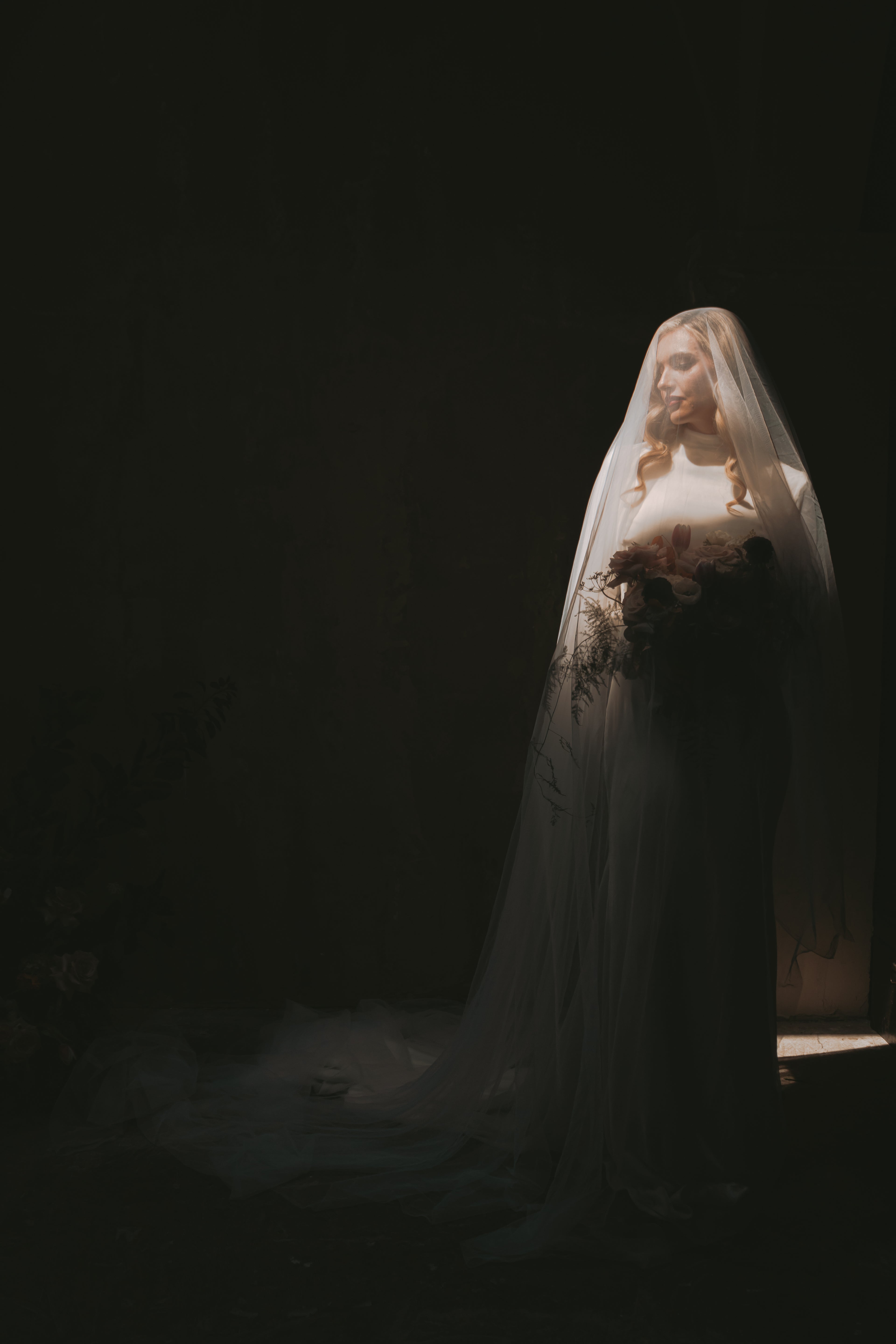 Woman in a long, white long sleeve wedding dress with a veil in a dimly lit setting